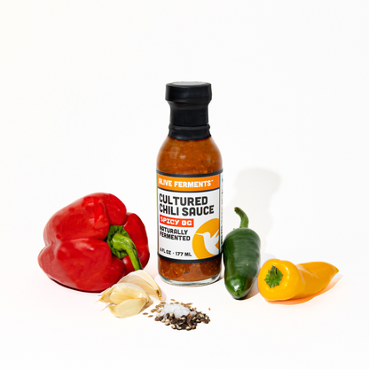 Bottle of cultured chili sauce with peppers and garlic on a white background