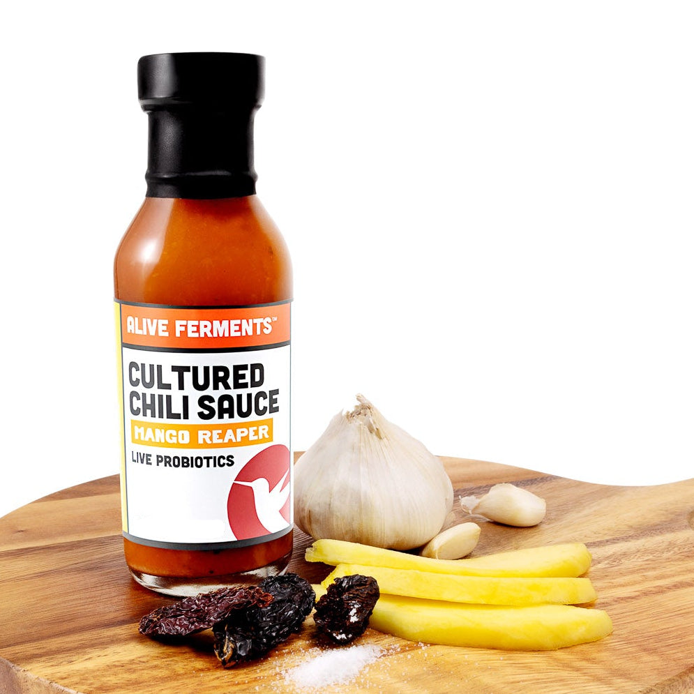 Bottle of Cultured Chili Sauce on a wooden cutting board with ingredients